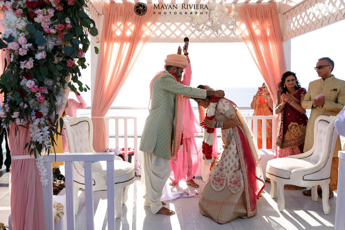 HinduGroomDrapesFlowersAroundBowingBride