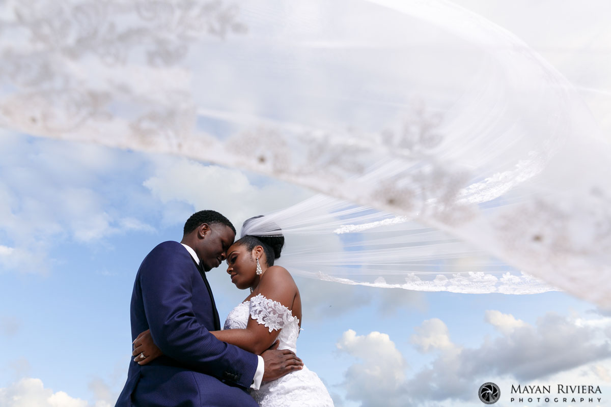 NewlywedsPoseOnBeachUnderFloatingVeil