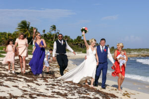 WeddingPartyWalksWithCheeringNewlywedsOnBeach