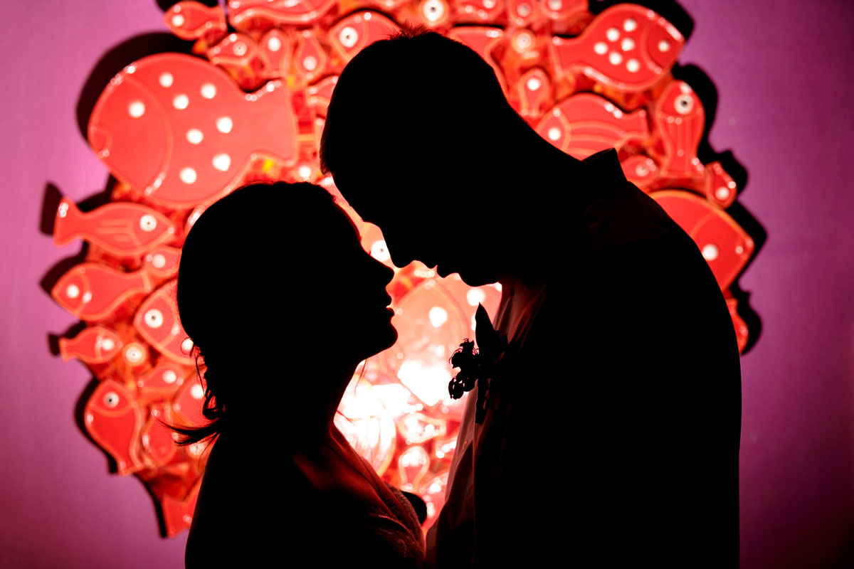 NewlywedsEmbraceShilouettedByWallArt