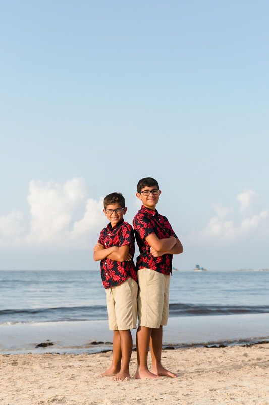 SmilingSonsStandBackToBackOnBeach