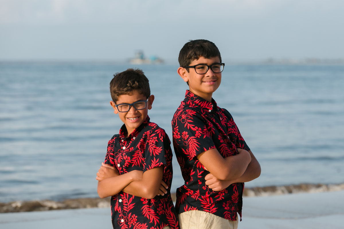 SmilingSonsStandBackToBackOnBeach