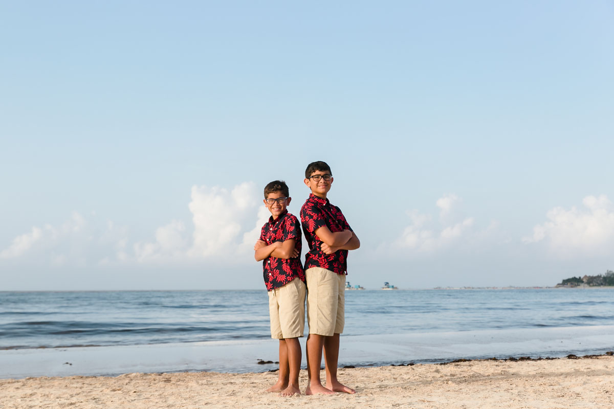 SmilingSonsStandBackToBackOnBeach