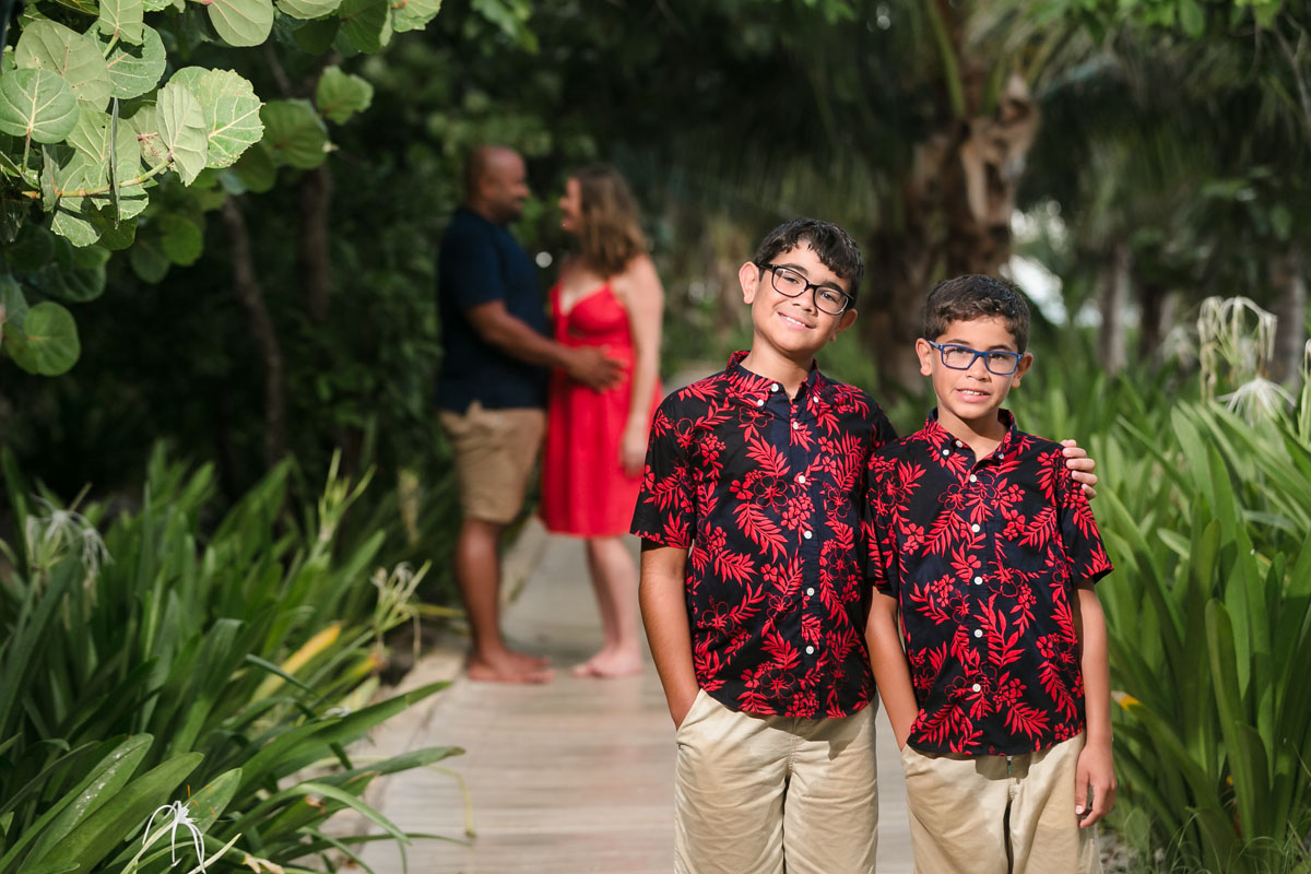 SmilingBoysPoseOnPathWithParentsInBackground