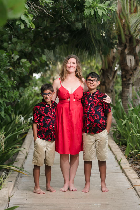 SmilingMomWithArmsAroundSonsStandOnPathway