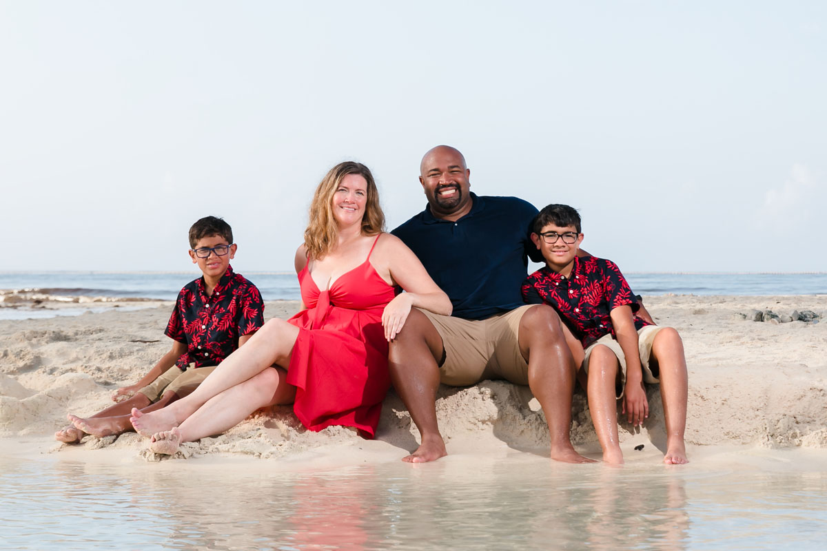 SmilingFamilySitsOnBeachBesideShallowTidePool