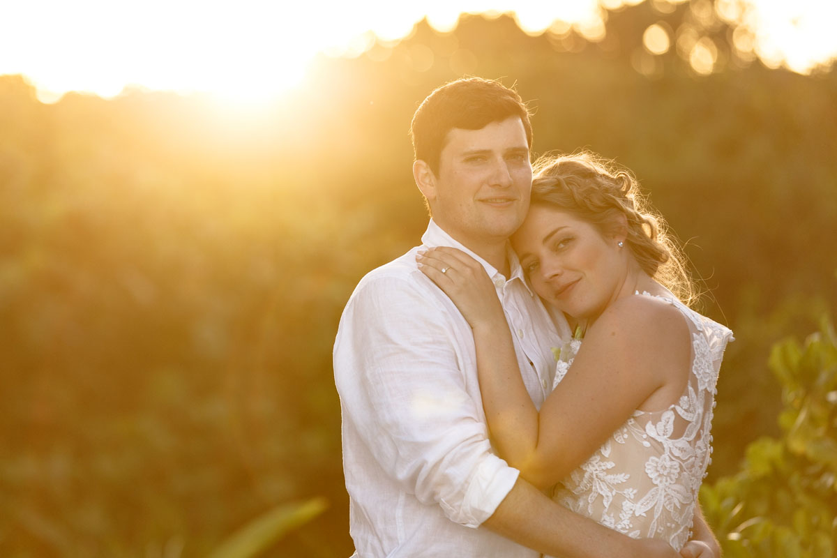 NewlywedsEmbraceOnBeachInSunsetGlow