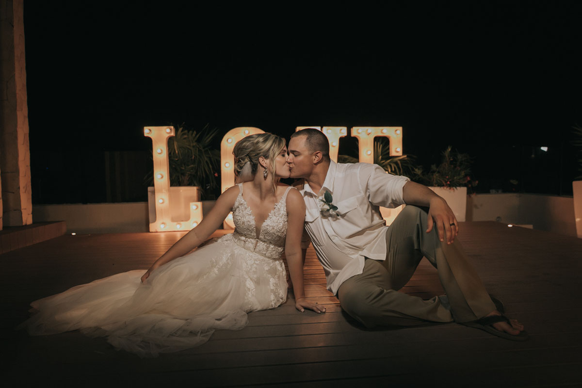 BrideAndGroomKissInFrontOfLoveSign