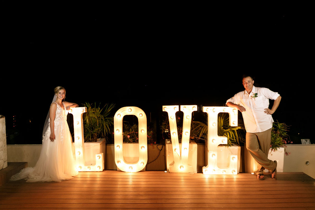 BrideAndGroomLeanOnLoveSign