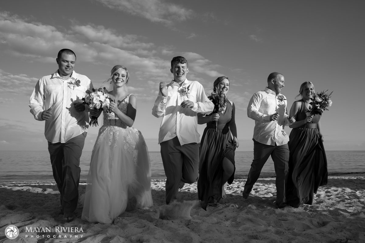 NewlywedsRunWithAttendantsOnBeach