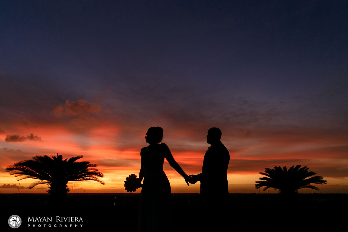 NewlywedsHoldHandsShilouettedBySpectacularSunset