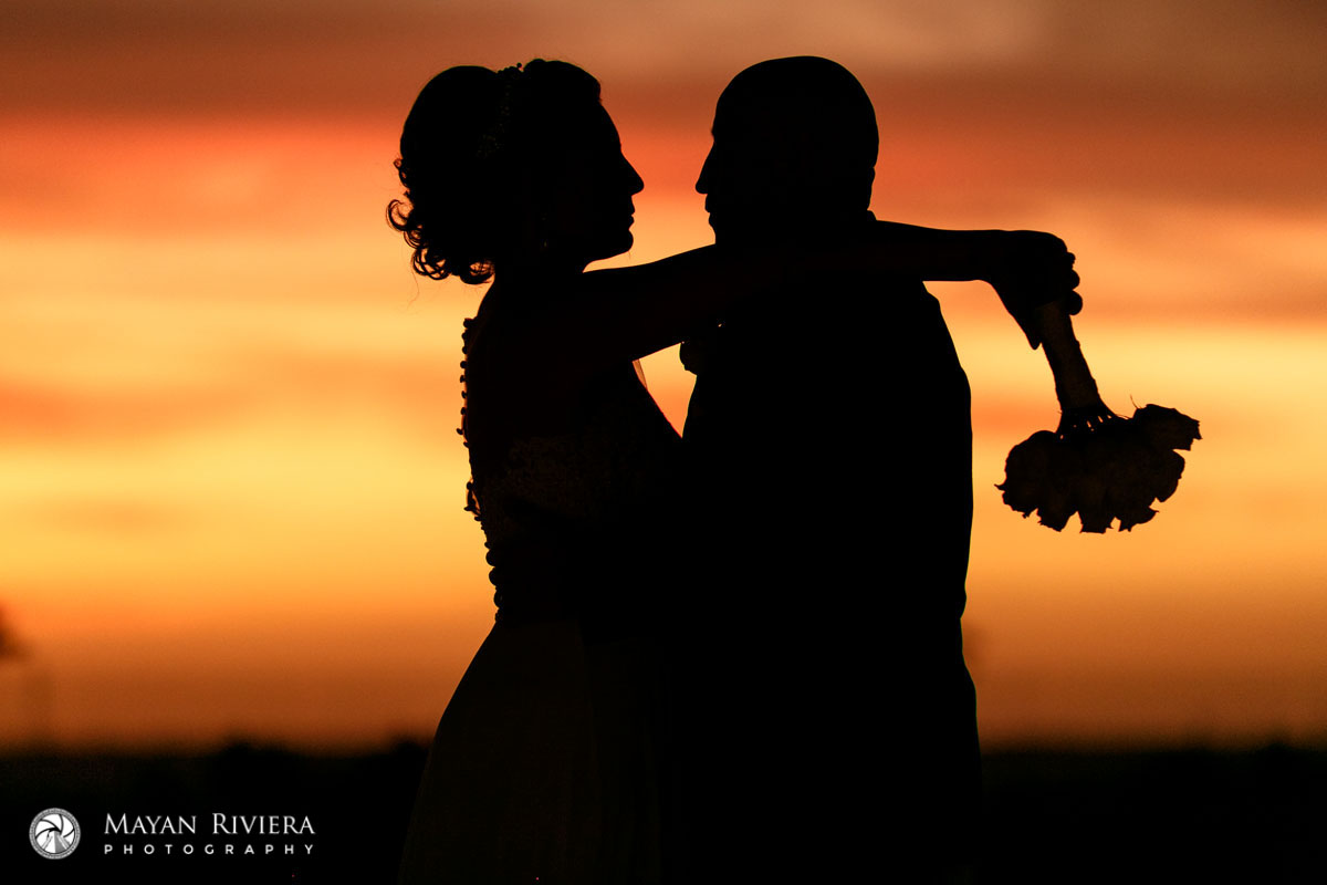 NewlywedsEmbraceShilouettedBySpectacularSunset