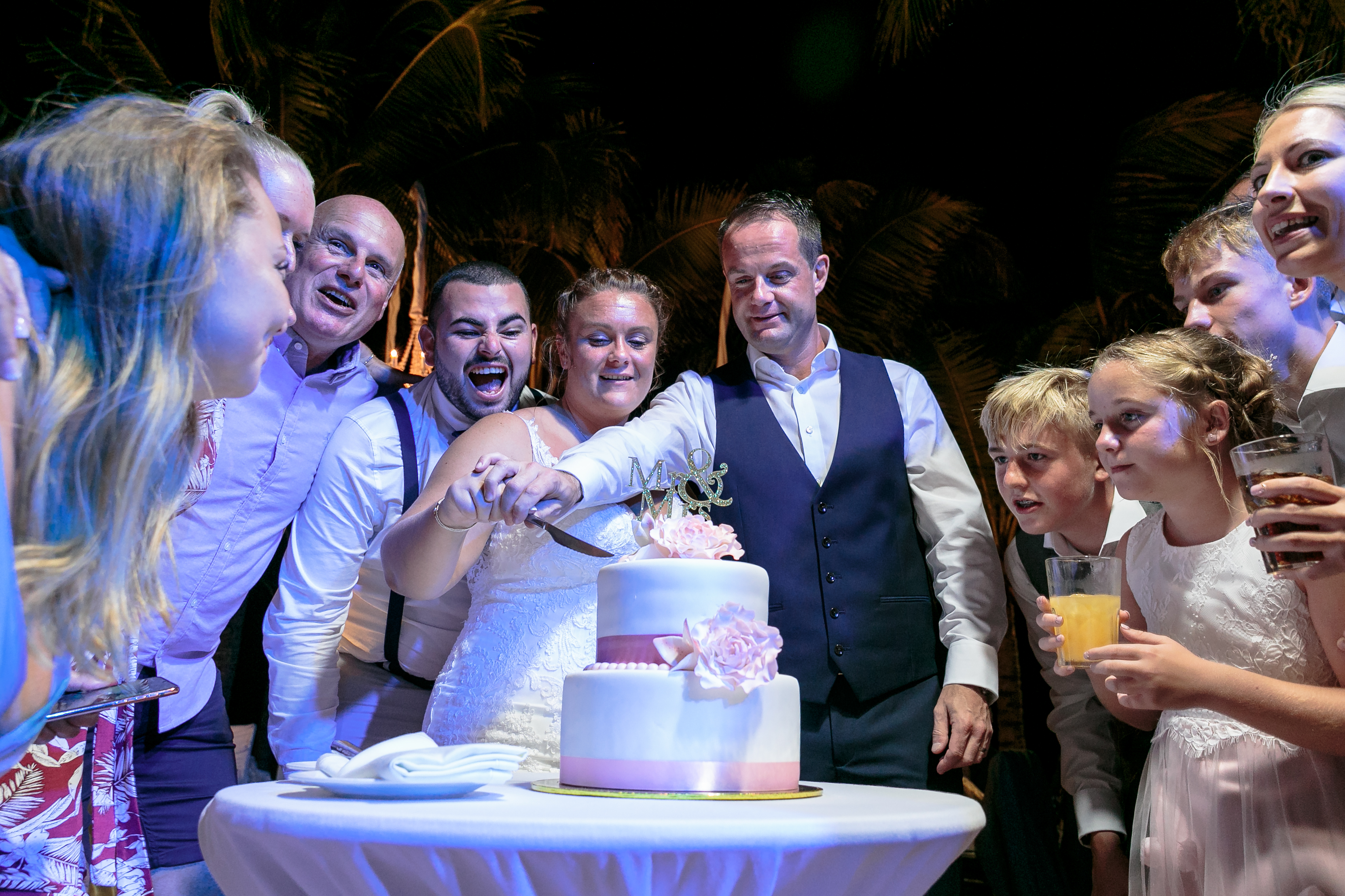 NewlywedsCutCakeWatchedByAdmirers