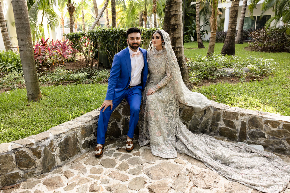 Newlyweds sit on stone garden wall smiling