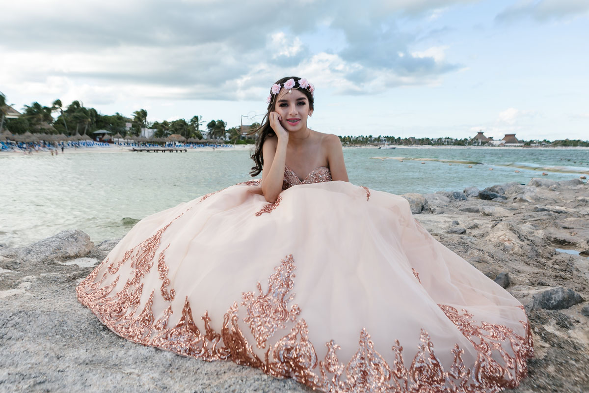 Quinceanera girl smiles sitting on beach rock