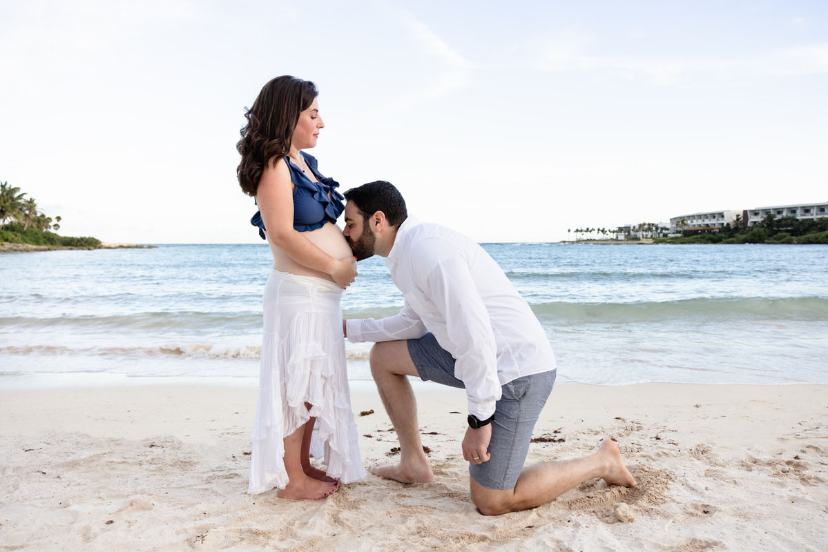 Expectant Dad kisses Mom's baby bump on the beach