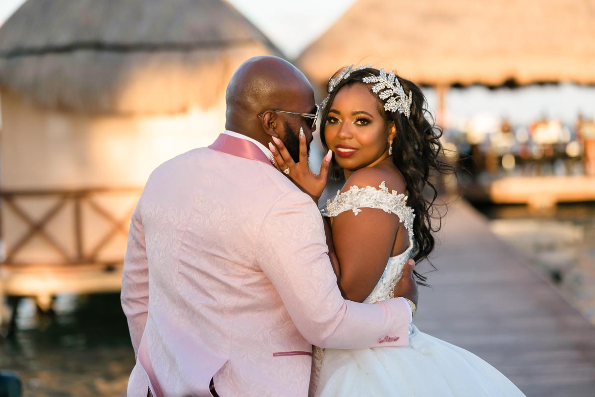Golden sunset light glows on newlywed bride looking over her husbands shoulder