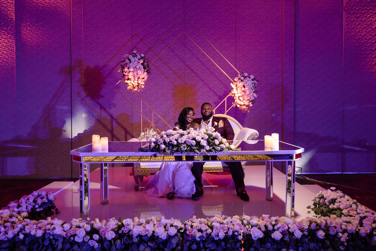 Newlyweds sit at head table decorate with elaborate flowers