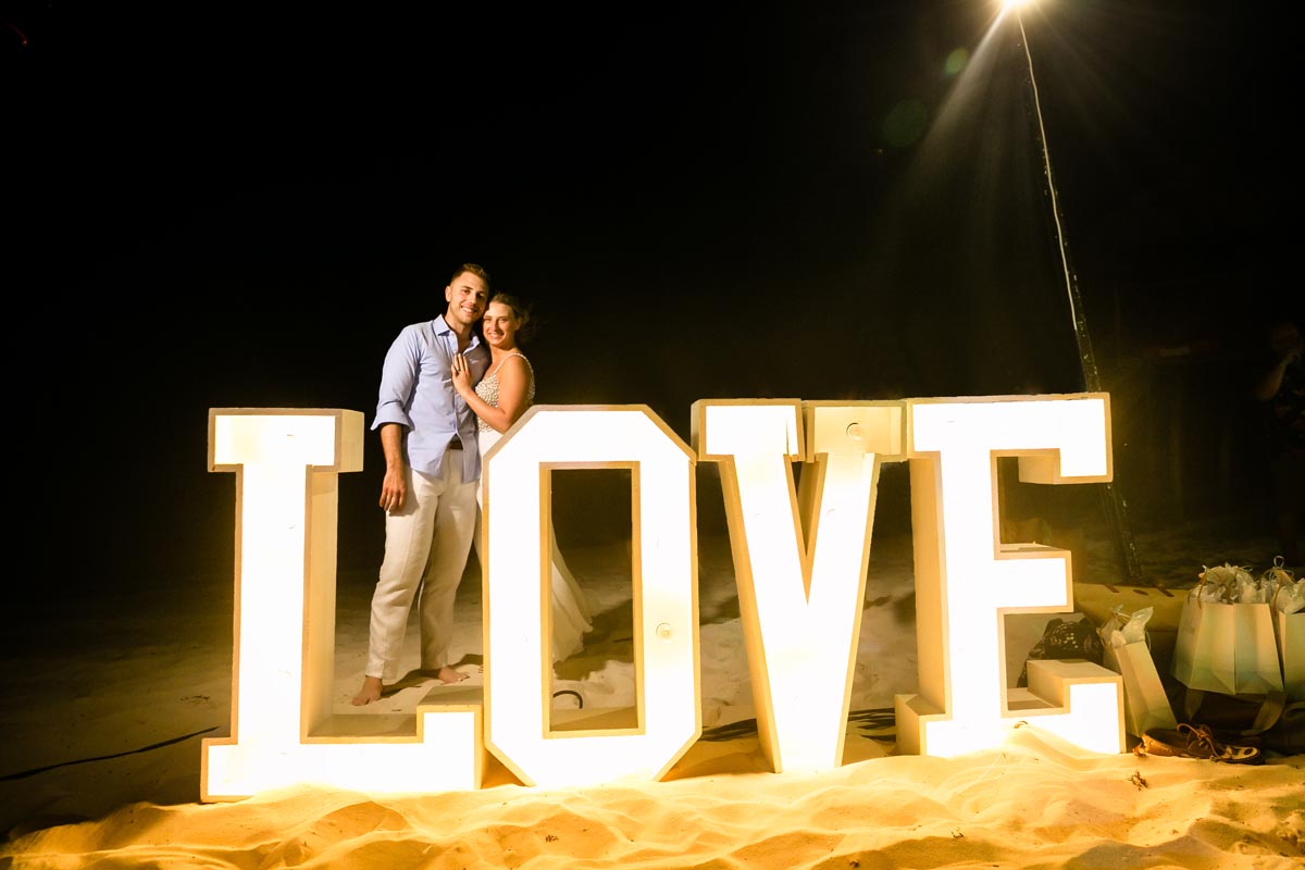 SandosPlayacarNewlywedsEmbraceByLoveSign