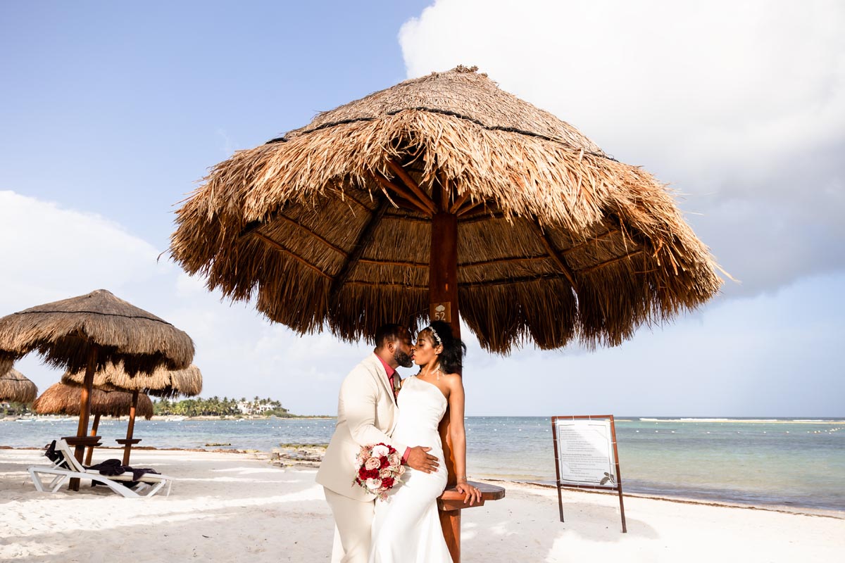 Newlyweds kiss under a beachside palapa