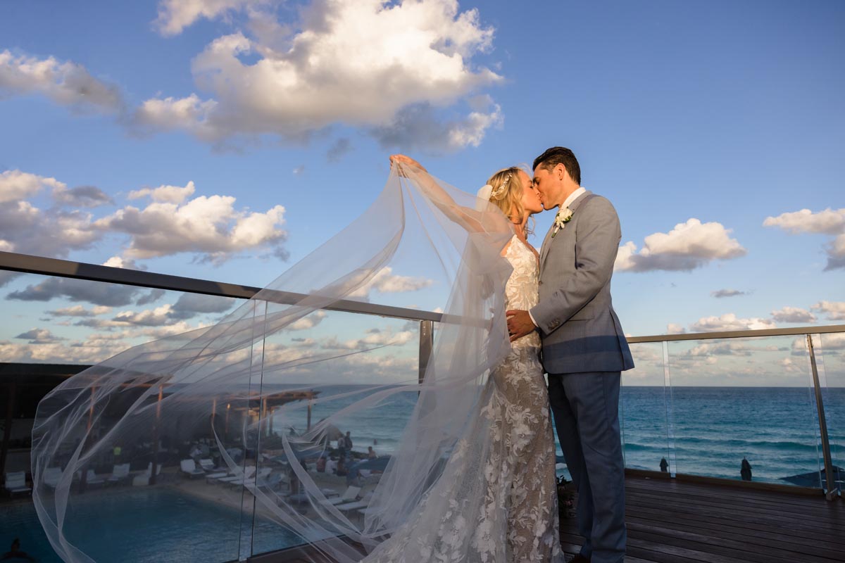 Newlyweds kiss with bride's veil billowing in the sunset