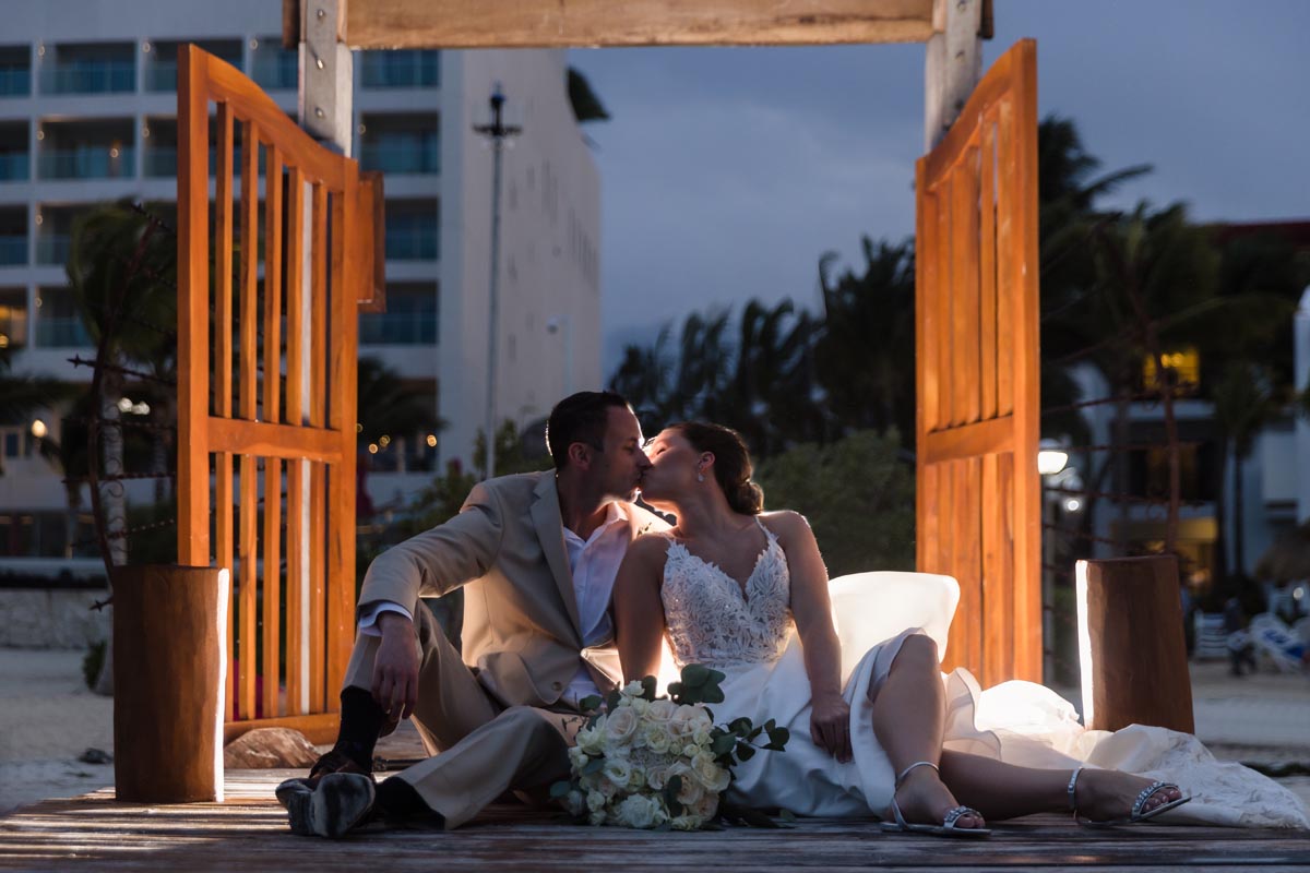 Newlyweds kiss sitting on deck framed by wooden slat doors