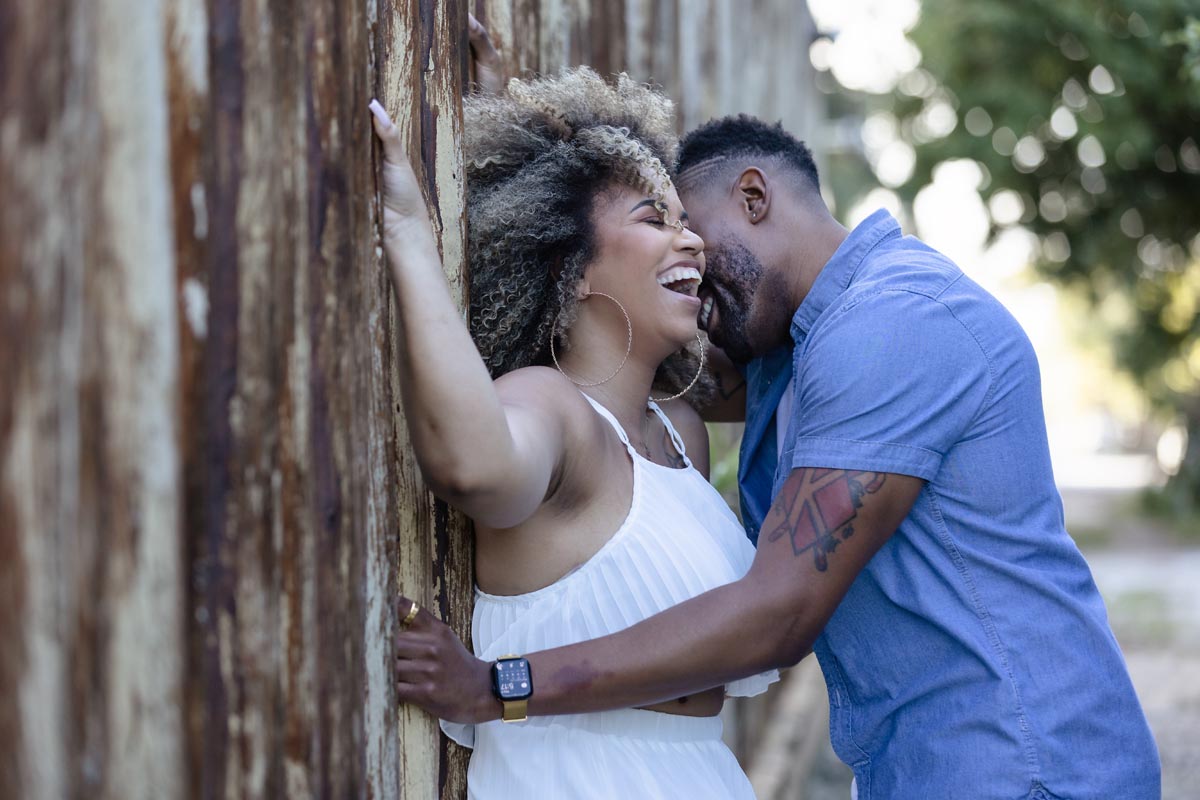Newly engaged couple embrace against reed wall
