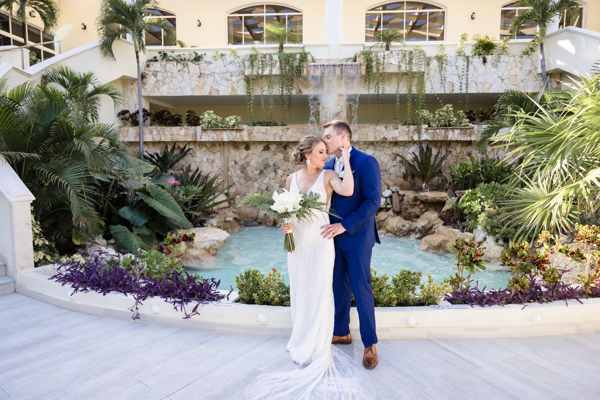 Wedding couple embrace in front of resort's rock pool