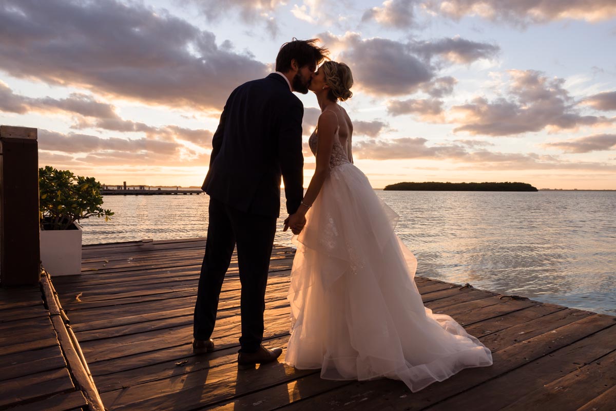 Newlyweds kiss on the deck silhouetted by the golden sunset