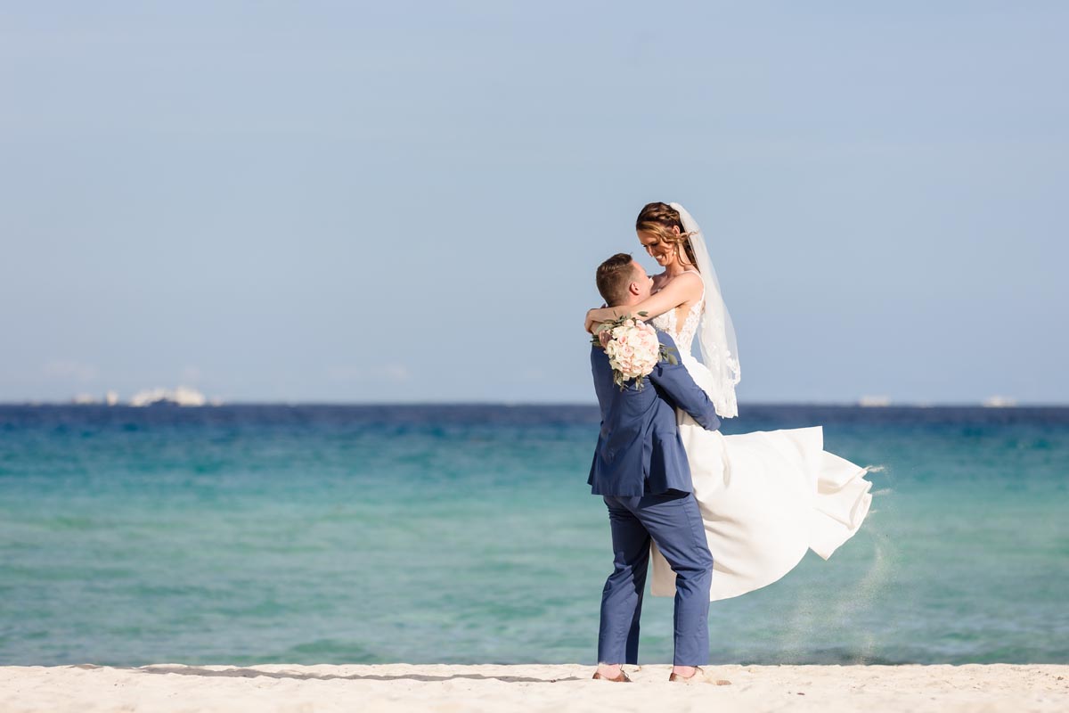 Newlywed groom twirls bride in his arms on the beach
