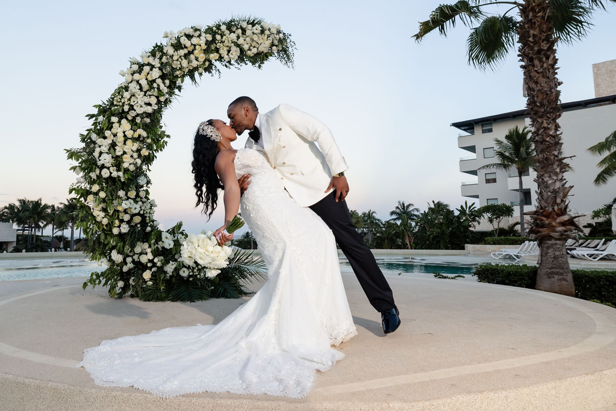 Newlywed groom dips his bride in a kiss, framed by an opulent floral ring