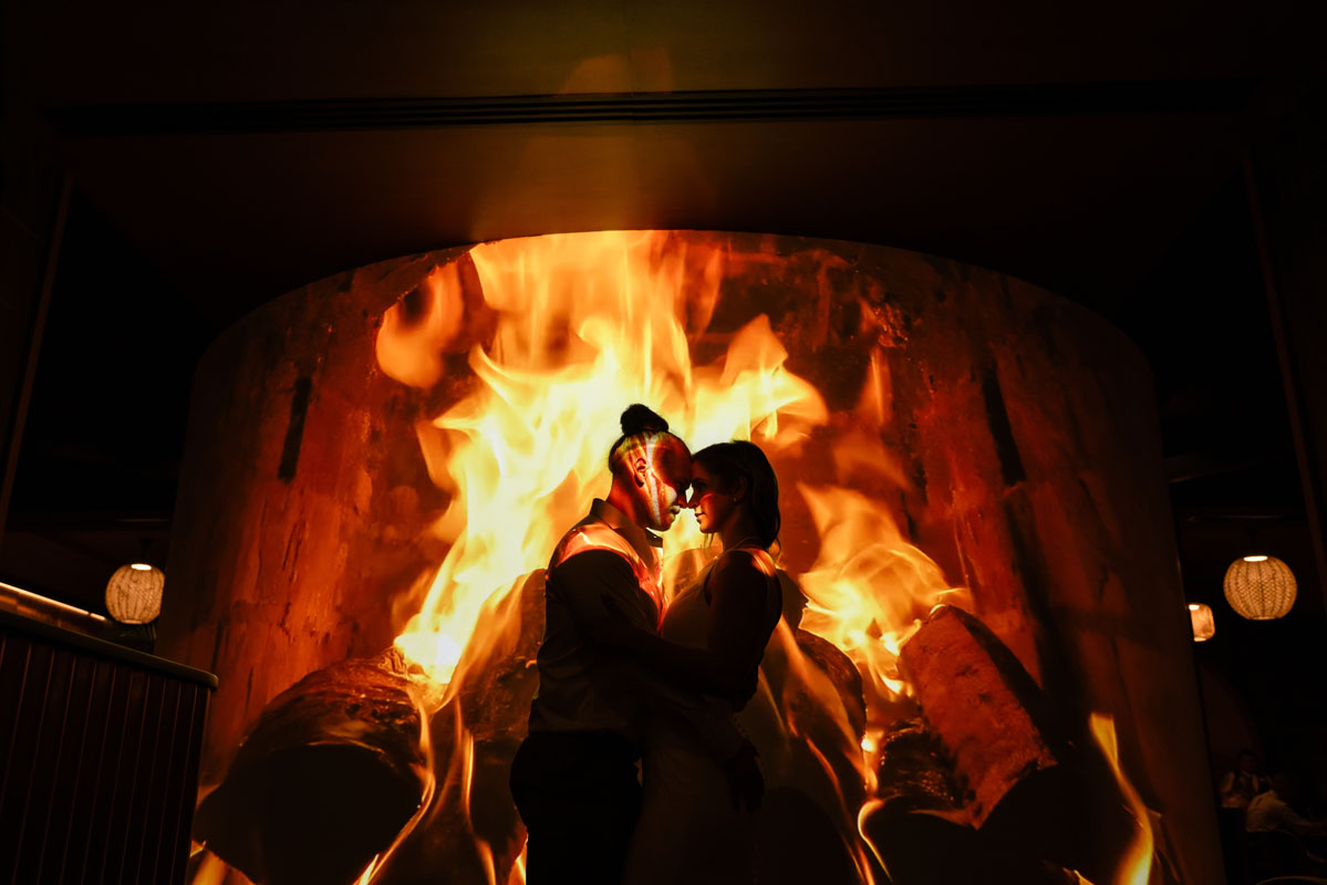 Newlyweds kiss lit up by a fire's flames