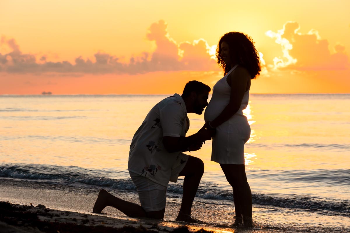Expectant Dad kisses Mom's baby bump at sunrise on the beach