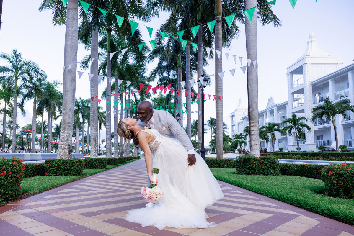 Newlywed groom dips his bride in a kiss on the palm lined boulevard
