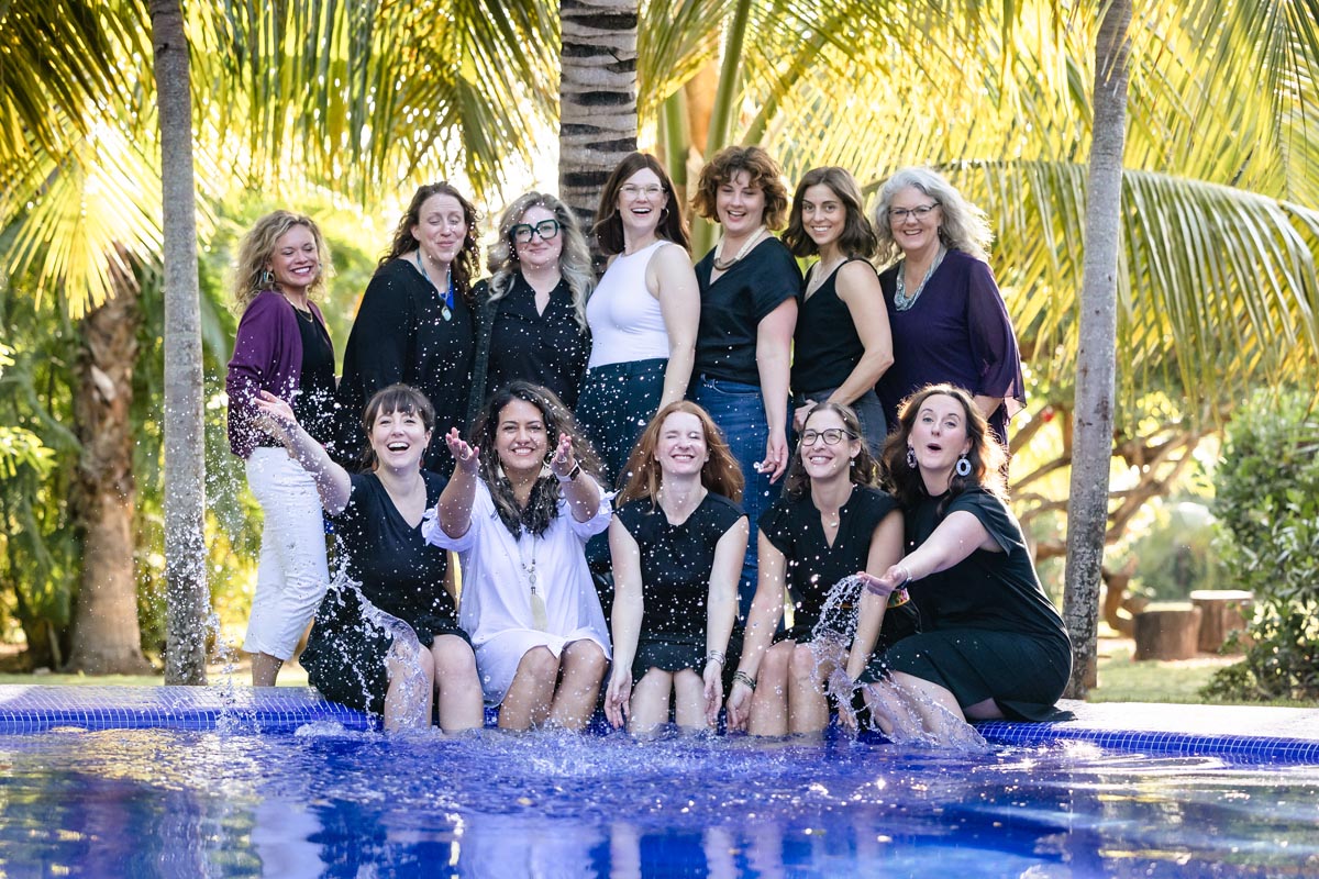 Ladies ham it up, splashing water while sitting on the pool edge