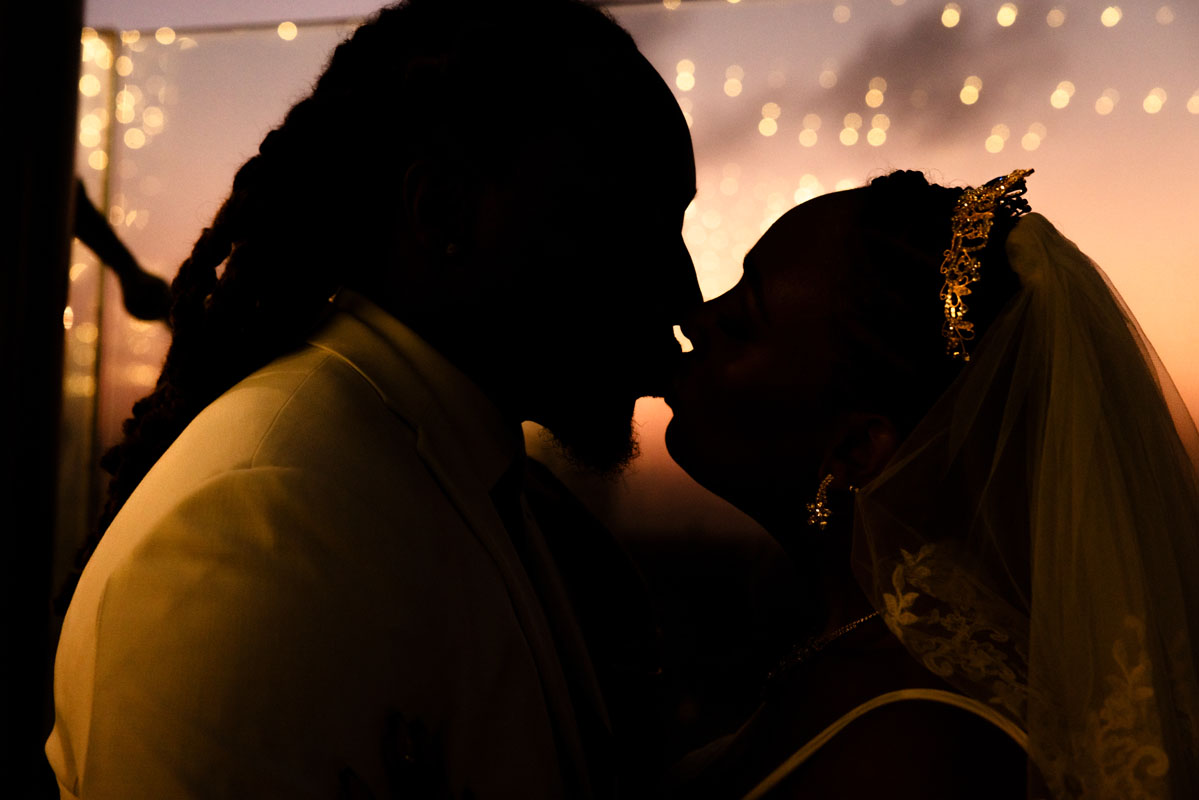 Newlyweds kiss shilouetted by the golden sunset