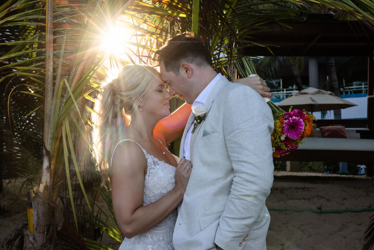 Newlyweds nuzzle foreheads together in a glowing starburst of the setting sun