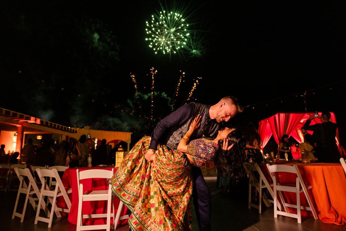 Groom dips his Hindu bride in a kiss under a shower of fireworks lighting up the sky