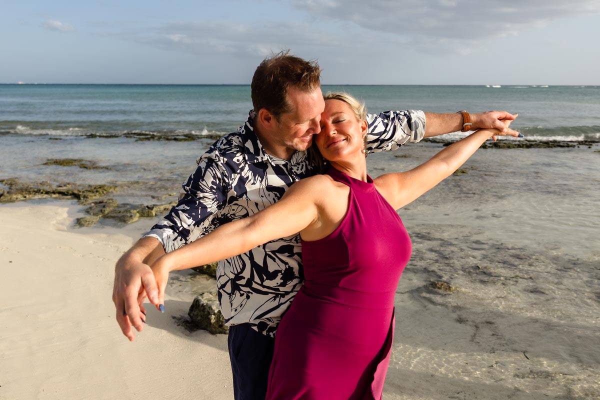 Newly engagement couple dance on beach with arms outstretched
