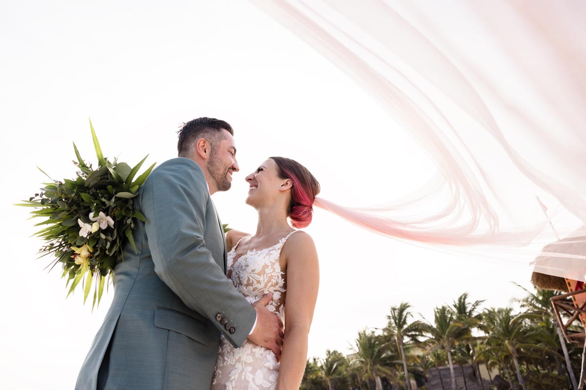 Newlyweds smile in an embrace under a billowing veil