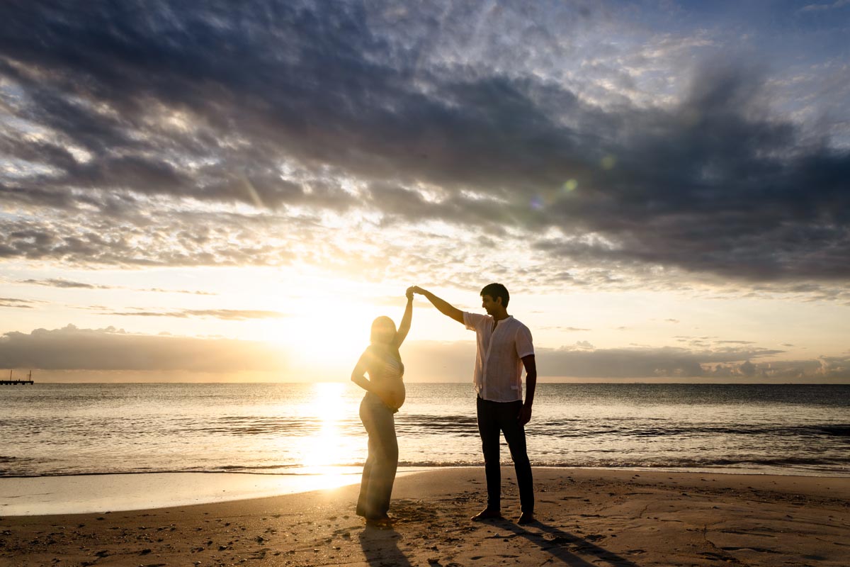 Expectant parents dance on beach at sunrise