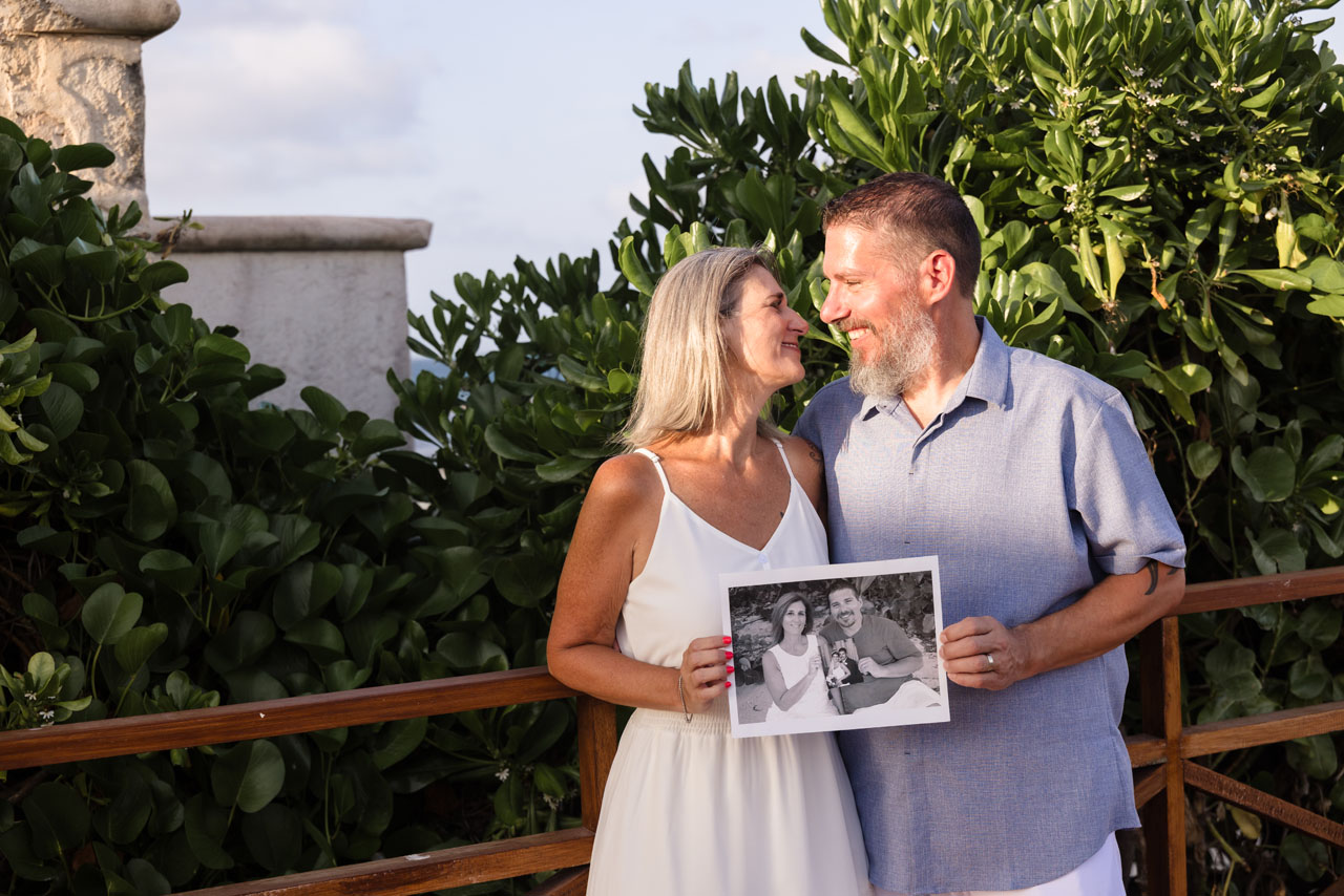 20th Anniversary couple hold photo of them on their wedding day and again on their 10th Anniversary